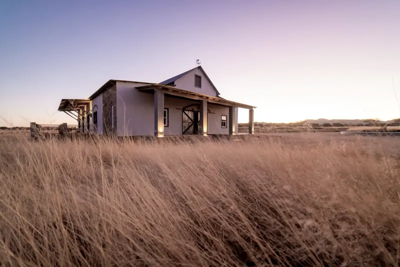 A farm cottage with a deep verandah in tall golden grass at dusk