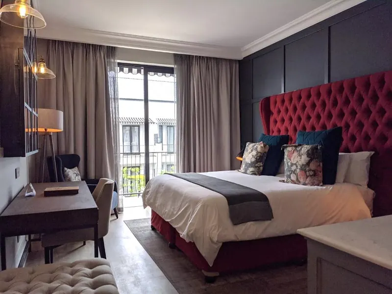 A hotel room with a deep red headboard and tall windows
